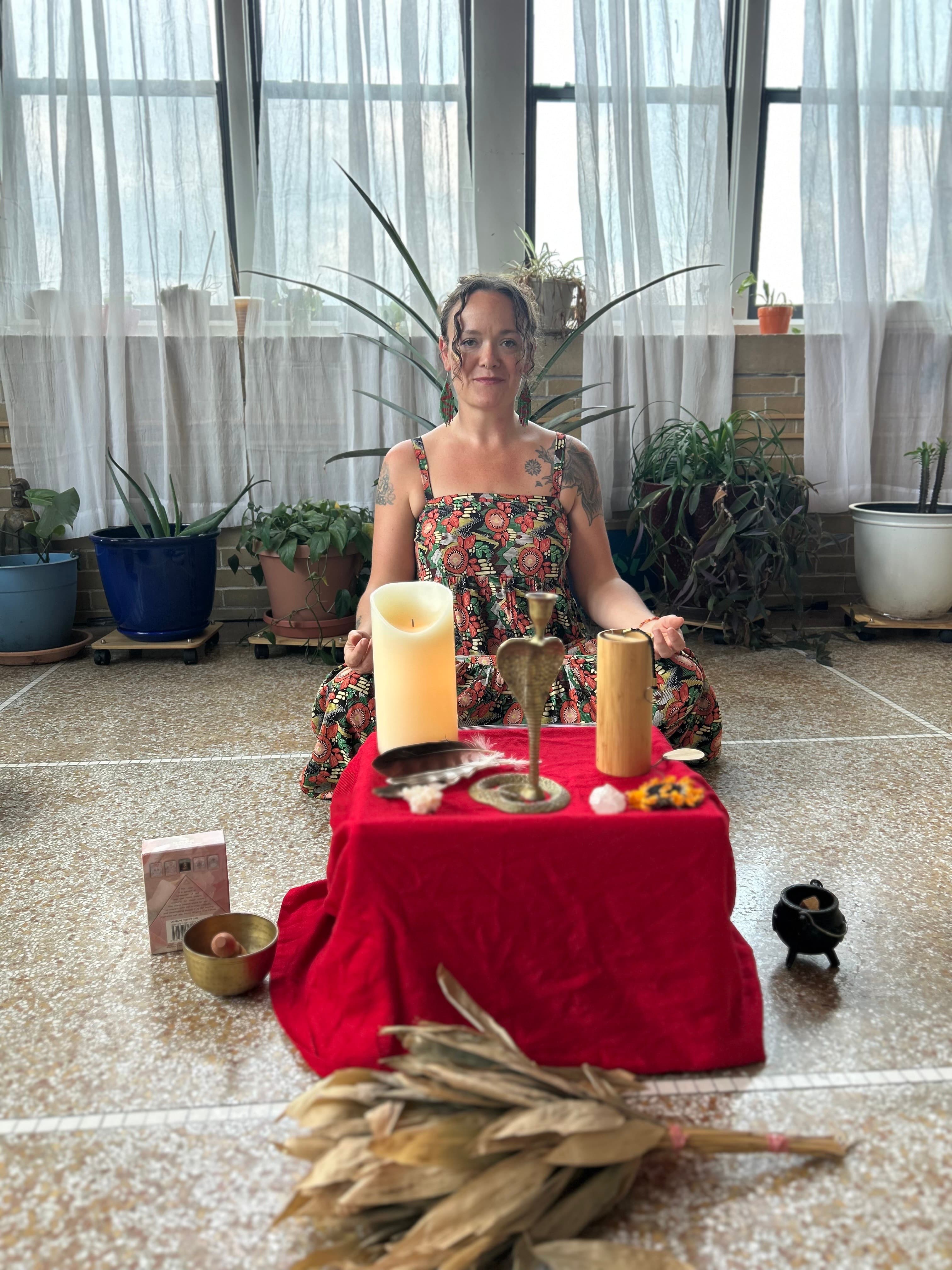 Kristina, founder of Kristina Medicina, seated at her botanical altar with candles, brass vessels, and plants