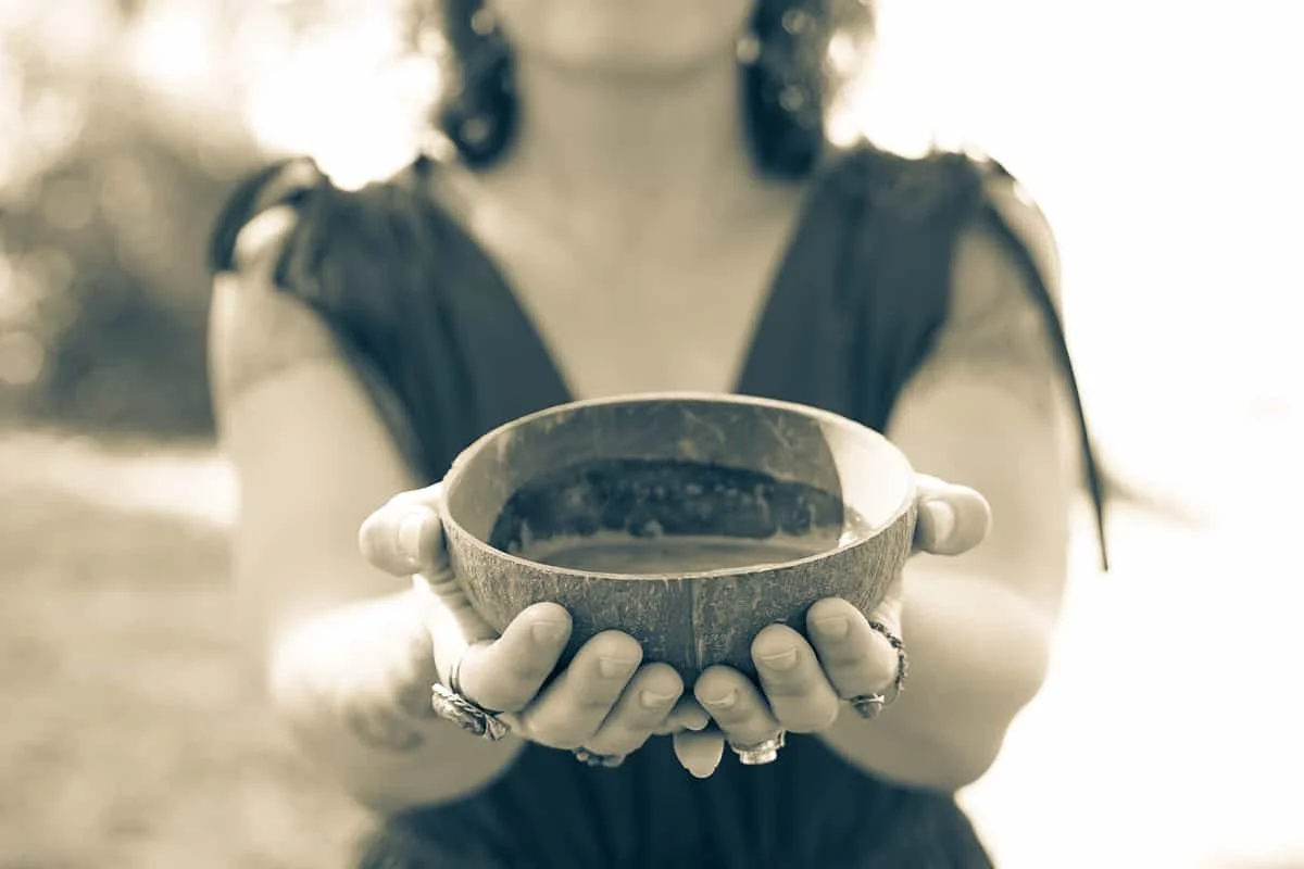 Two hands offering a wooden bowl of ceremonial cacao