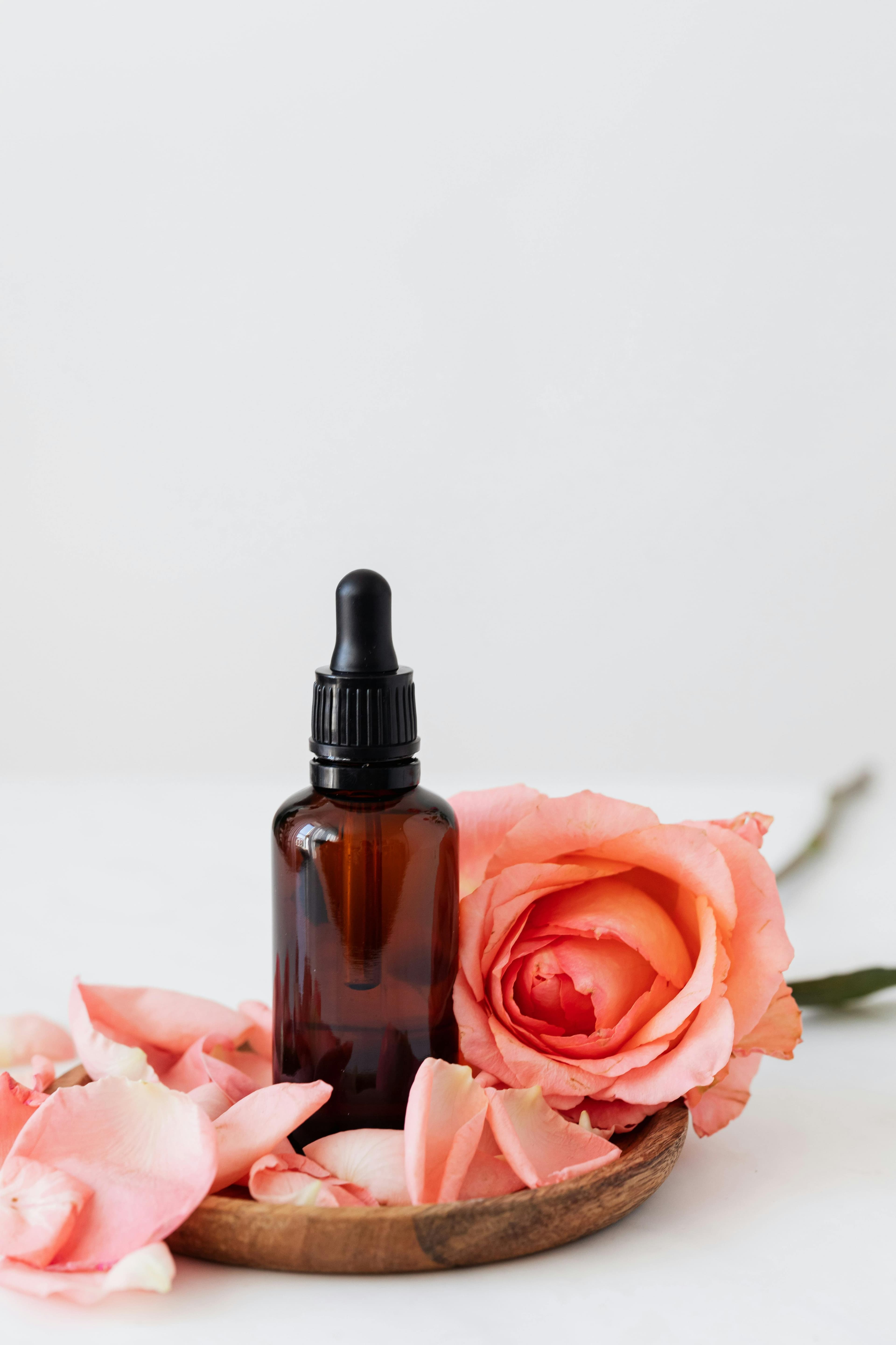 An amber glass dropper bottle beside a fresh rose on a wooden dish